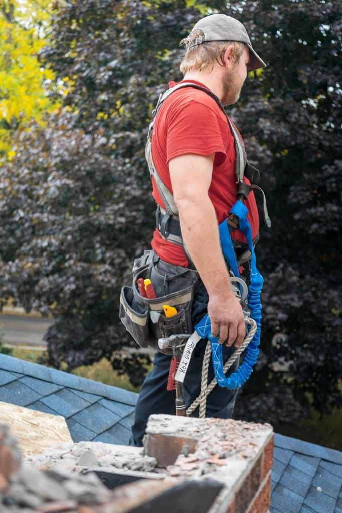 A constructionTécnico revisando el conducto de una chimenea en el tejado worker with safety gear stands on a residential rooftop, inspecting a chimney.